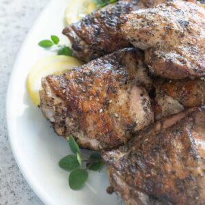 Grilled chicken thighs on a platter with lemon and oregano
