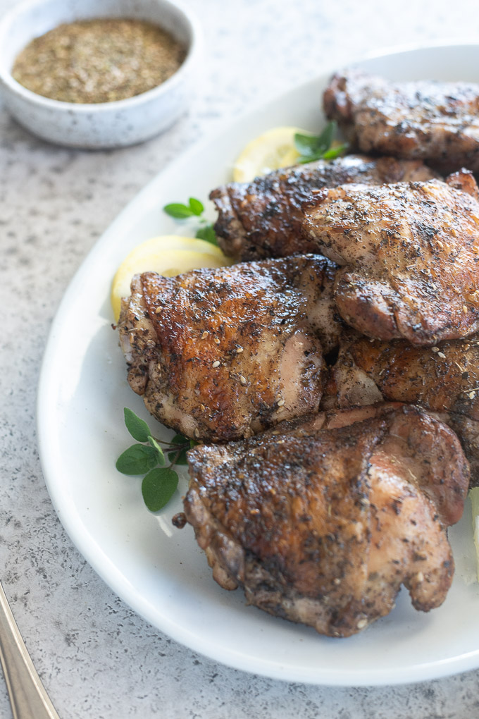 Platter of za'atar grilled chicken thighs with a bowl of seasoning nearby