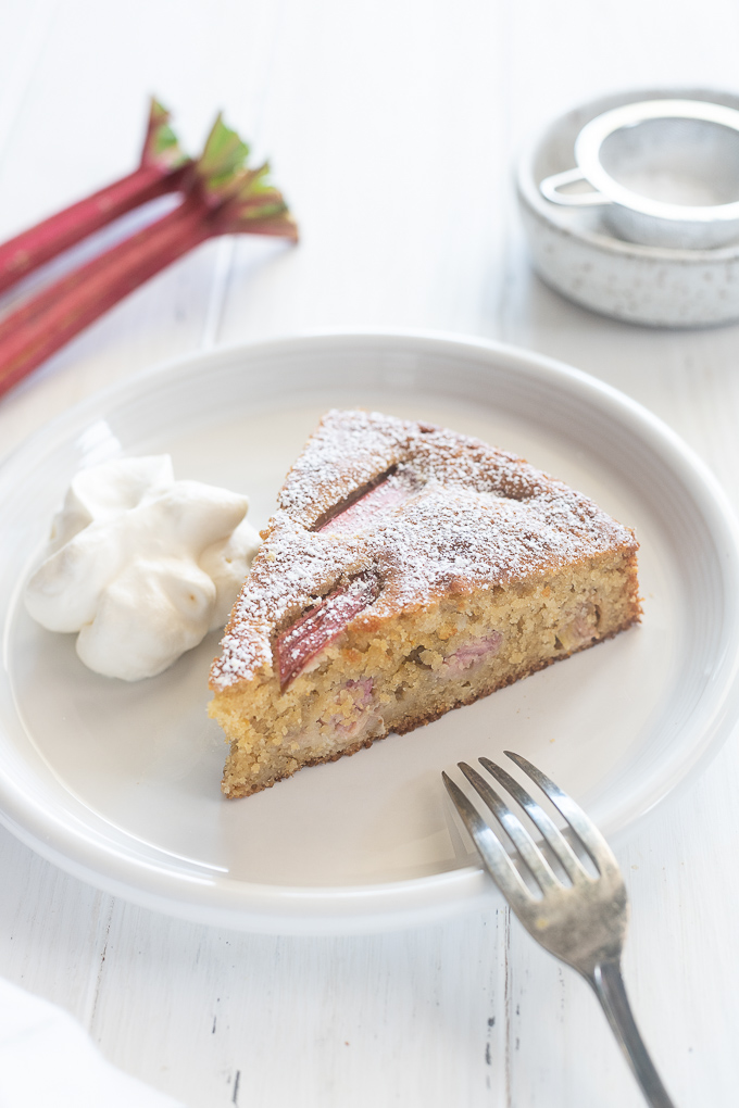 Slice of rhubarb cake on a plate with whipped cream