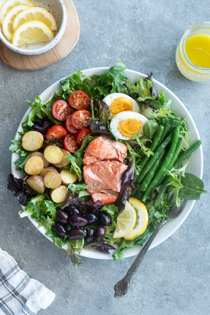 Salmon nicoise salad on a white plate with lemon slices and a fork