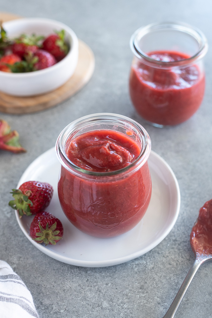 Jar of rhubarb and strawberry jam with strawberries around it