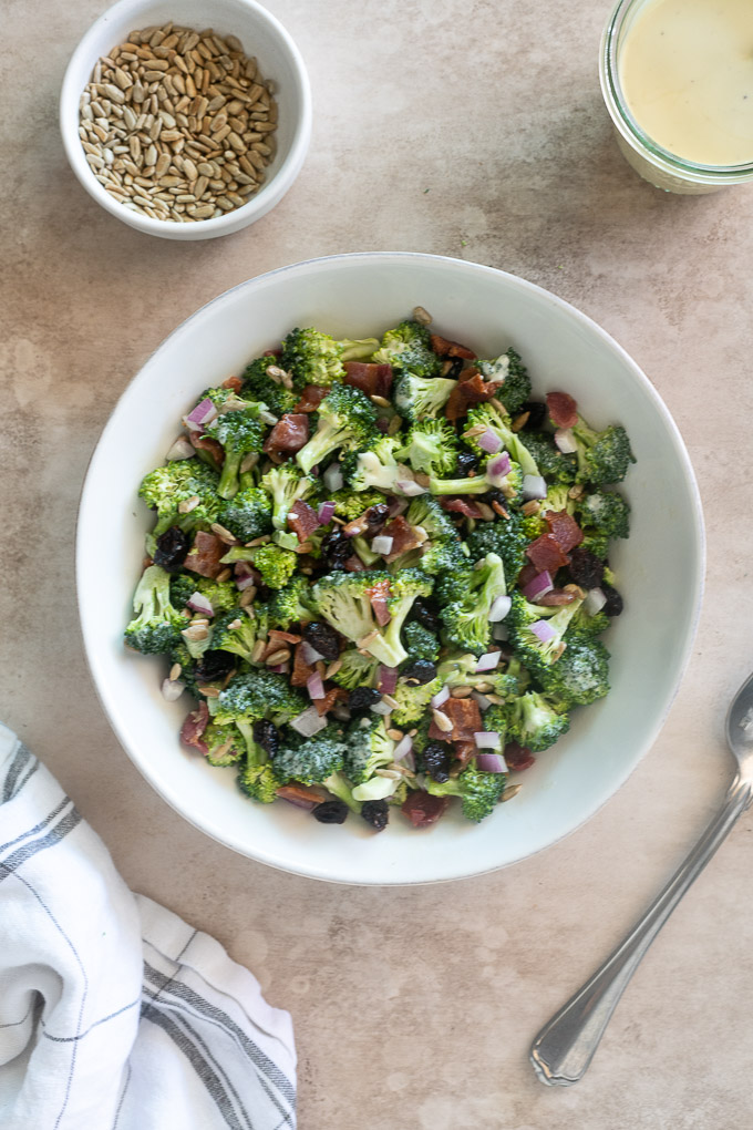 Broccoli salad recipe with bacon in a white bowl with a spoon alongside