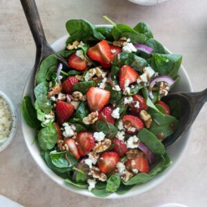 Strawberry spinach salad in a bowl with salad servers