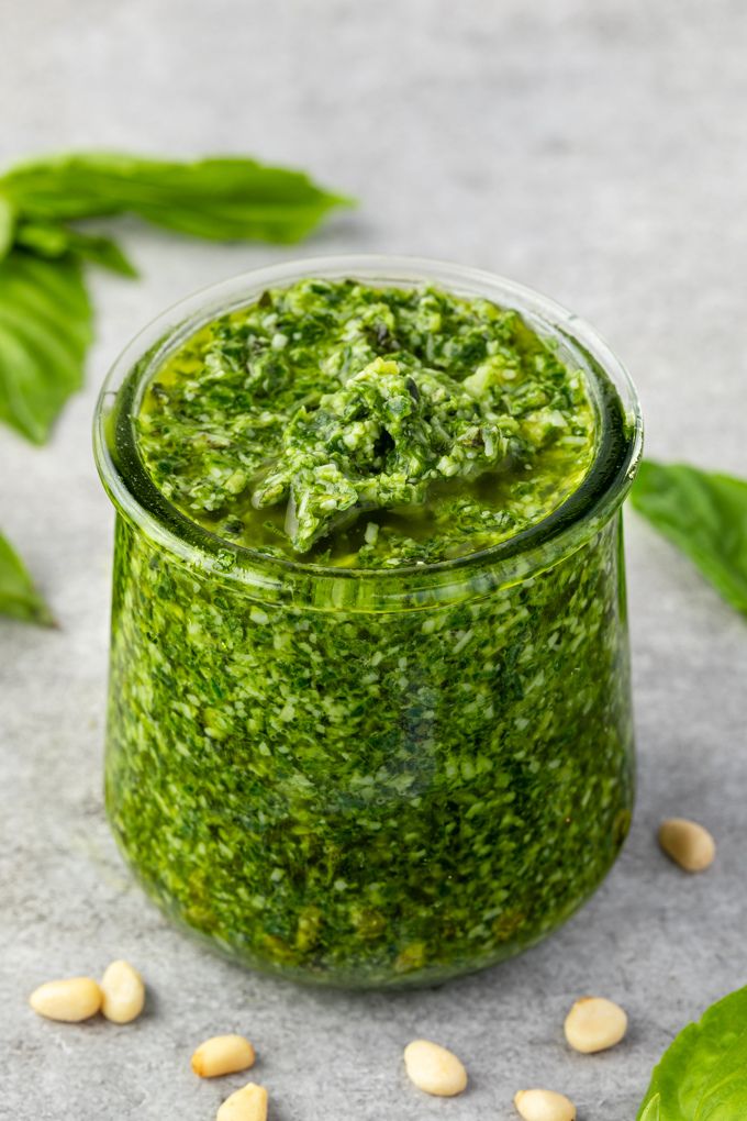 Basil pesto in a jar with pine nuts and basil leaves around it