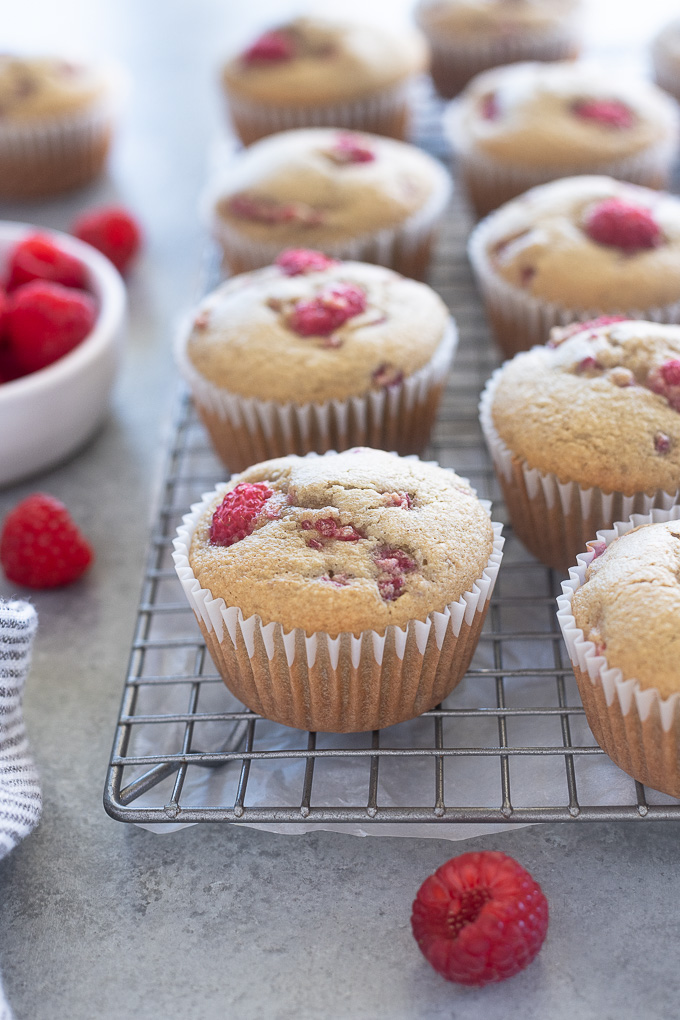 Raspberry muffins on a wire rack with a bowl of raspberries alongside
