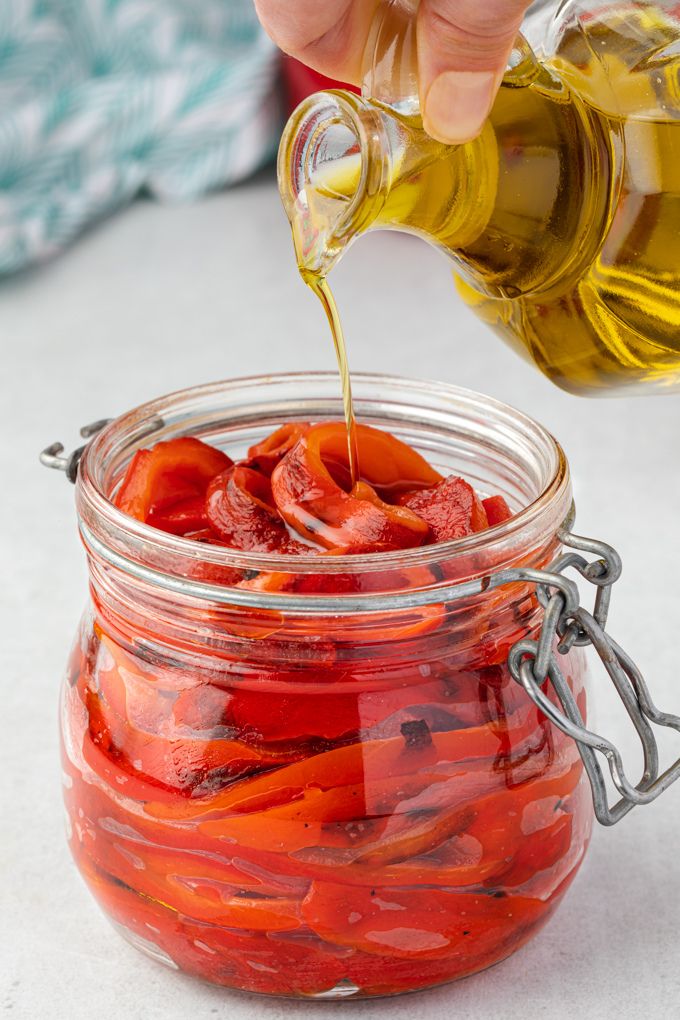 Roasted red peppers in a jar with olive oil drizzling over the top