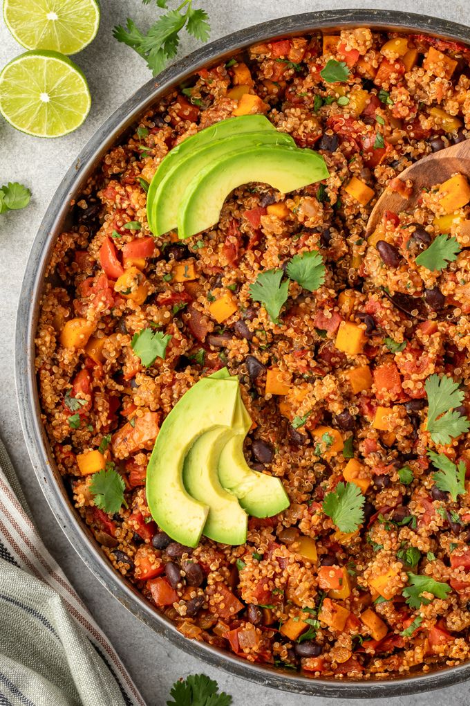 Mexican quinoa in a skillet with sliced avocado and cilantro leaves