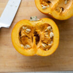 Pumpkin cut in half on a cutting board with knife