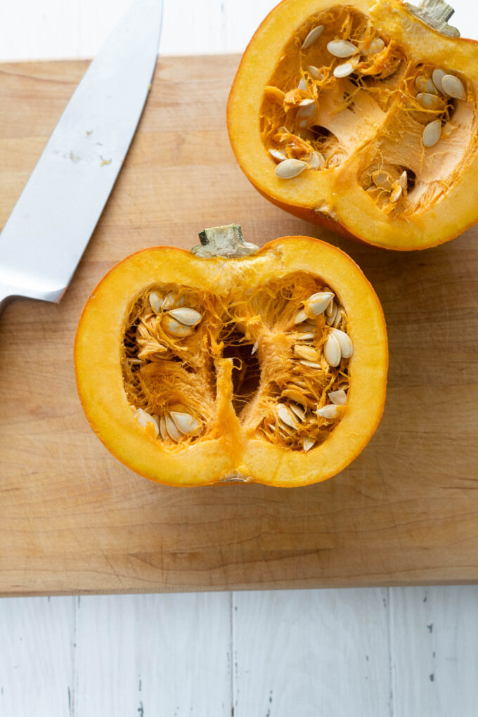 Pumpkin cut in half on a cutting board with knife