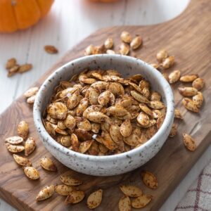 Roasted pumpkin seeds in a bowl on a cutting board