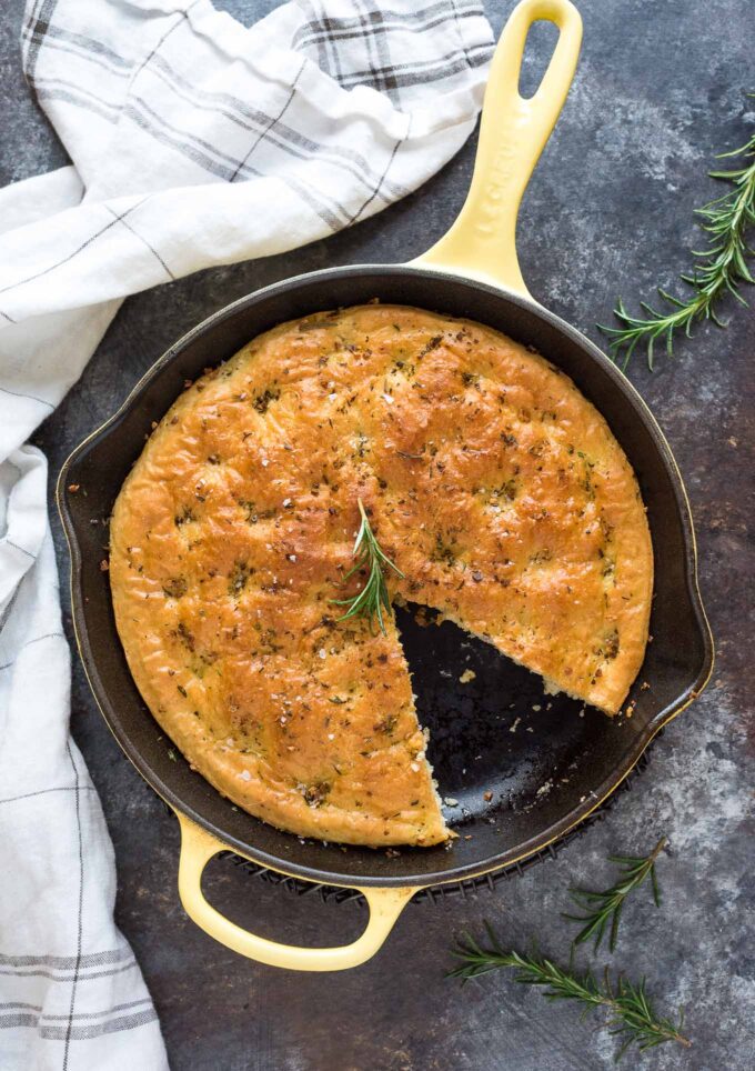 Rosemary focaccia bread in skillet with slice missing