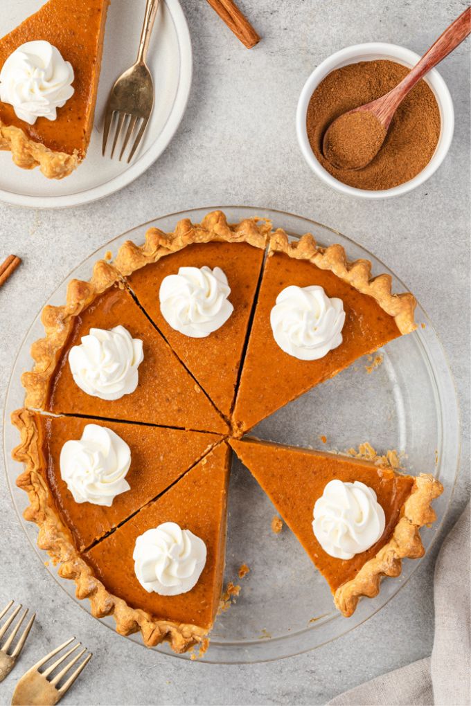 Homemade pumpkin pie in baking dish sliced with whipped cream