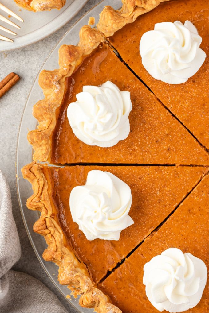 Homemade pumpkin pie sliced in pan with whipped cream