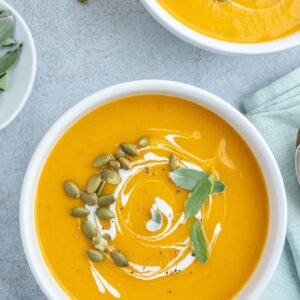 Roasted pumpkin soup in bowls with coconut milk and sage