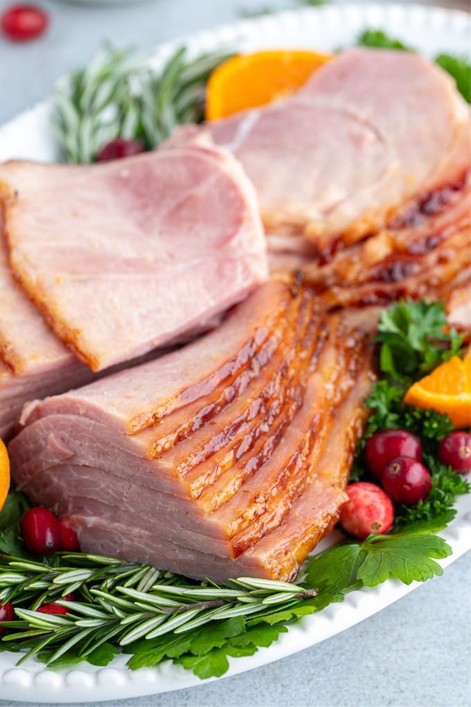 Crock pot ham sliced on a platter with herbs, cranberries and orange