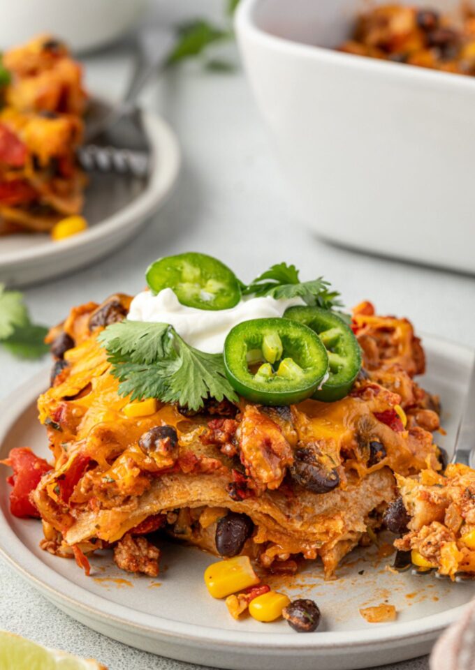 Serving of Mexican tortilla casserole topped with sour cream and jalapeno