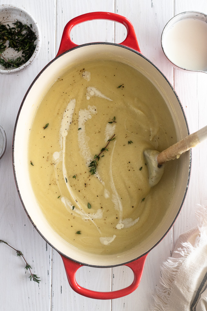 Parsnip soup in a dutch oven with a thyme sprig and wooden spoon