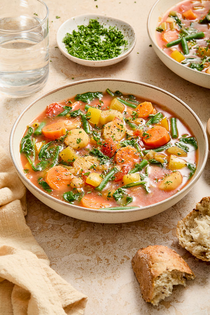 Instant pot vegetable soup in a bowl with bread and parsley garnish