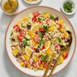Greek orzo salad in a bowl with salad servers.
