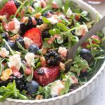 Berry arugula salad with goat cheese in a bowl with a fork digging in.