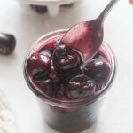 Spoonful of cherry compote over a jar.