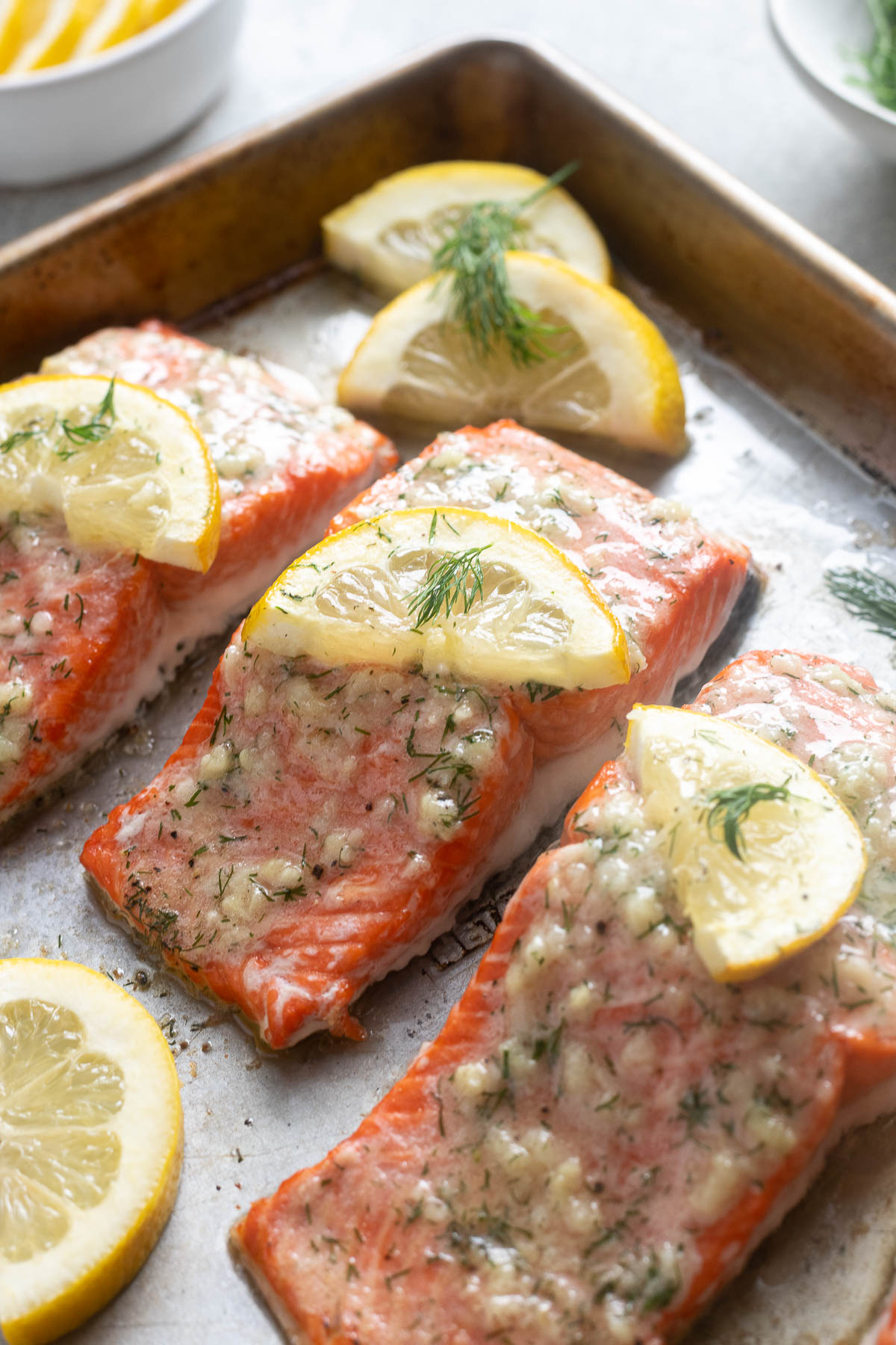 Garlic butter salmon on a baking sheet with dill and lemon.