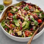 Italian chopped salad in a bowl with jar of dressing and basil.