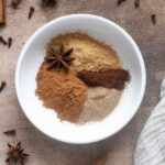 Spices for chai spice mix in a small white bowl.
