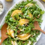 Arugula pear salad on a platter with wooden salad servers.