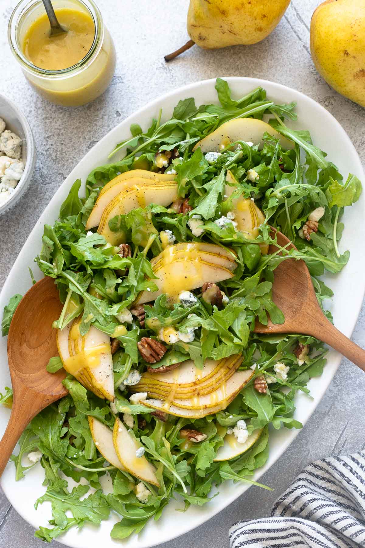 Arugula pear salad on a platter with wooden salad servers.