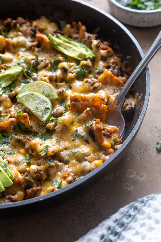 Ground beef enchilada casserole with serving spoon digging into skillet.