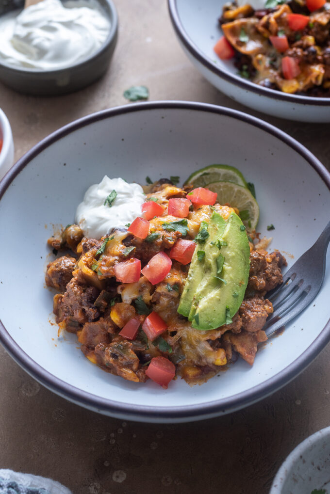 Serving of skillet enchiladas in a bowl with tomato, avocado and sour cream.