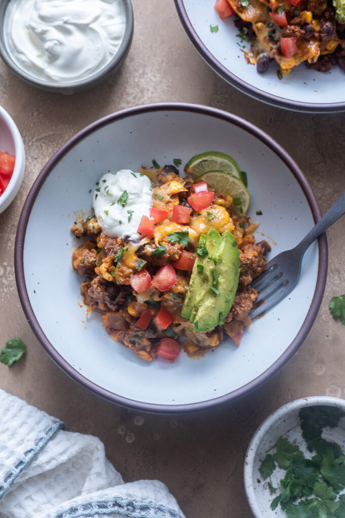 Serving of ground beef enchiladas skillet in a bowl with toppings.