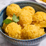 Scoops of Mexican sweet corn cake in a bowl with cilantro sprig.