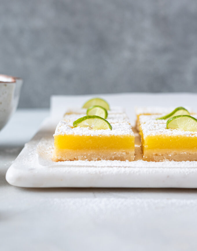 Key lime bars with powdered sugar and lime slice on top.