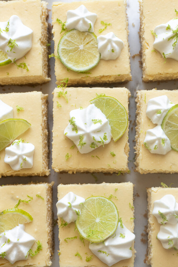 Cheesecake bars cut into squares with whipped cream, key lime zest and juice.