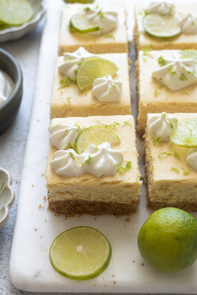 Key lime cheesecake bars with piped whipped cream and lime slices.