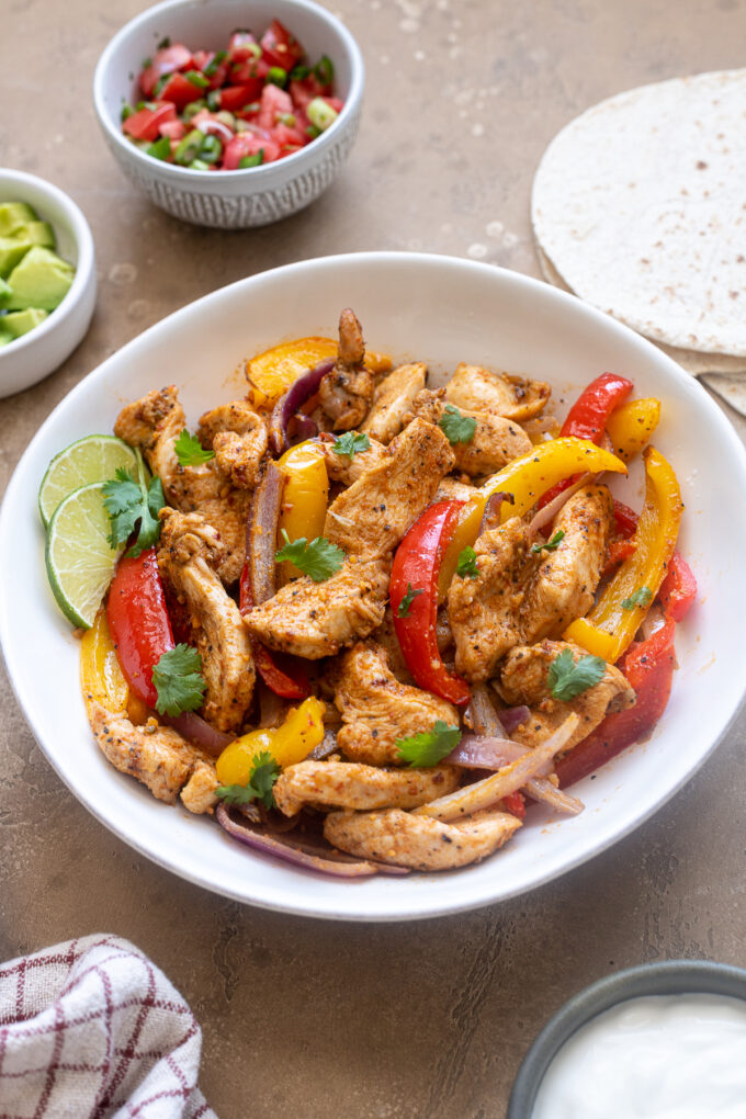 Air fryer chicken fajitas in a bowl with cilantro leaves.