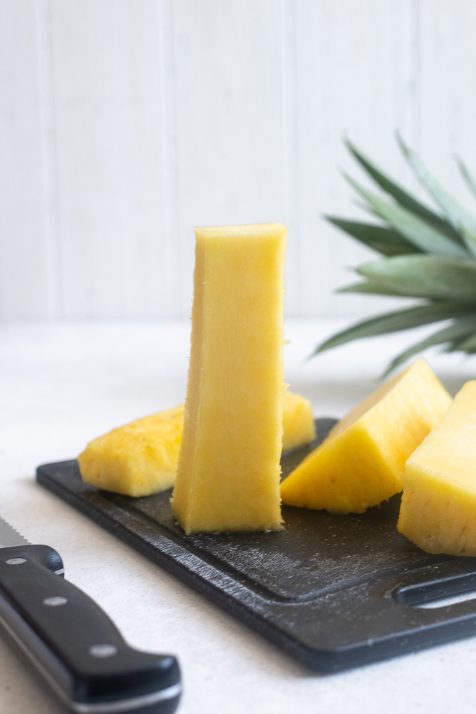 Pineapple core standing on cutting board with pineapple alongside.