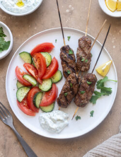 Kofta kebabs on a plate with tzatziki and vegetables.