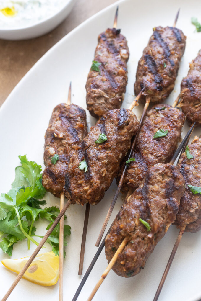 Grilled lamb kofta with wooden skewers on serving platter.