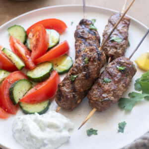 Lamb kofta kebabs on a plate with tzatziki and vegetables.