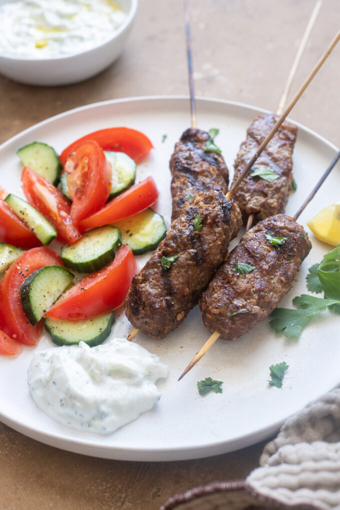 Lamb kofta kebabs on a plate with tzatziki and vegetables.