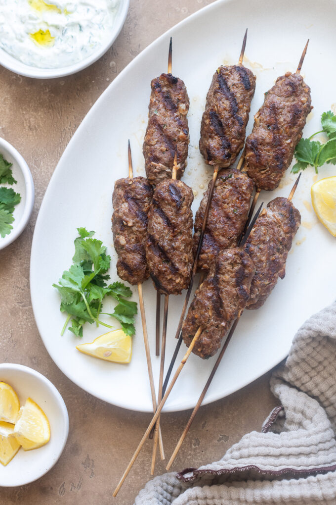 Lamb kofta kebabs on a serving platter with herbs and lemon.