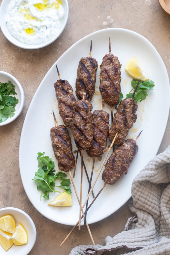 Lamb kofta on a platter with lemon and cilantro.