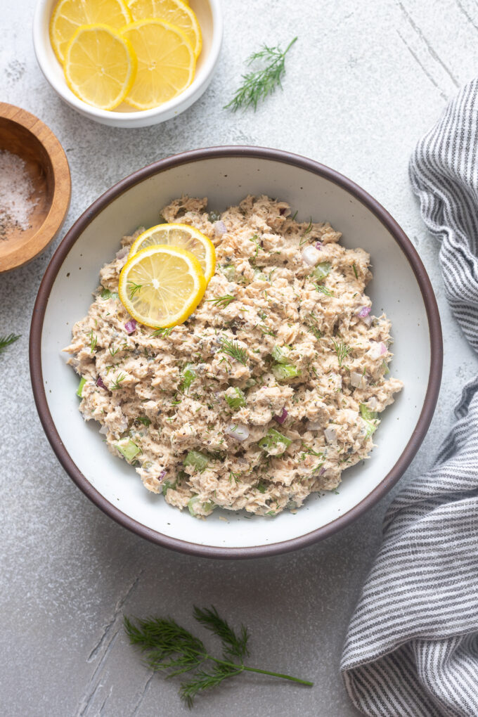 Salad with canned salmon in a bowl with lemon slices and dill.
