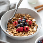 Almond butter granola in a bowl with berries and almond butter drizzle.