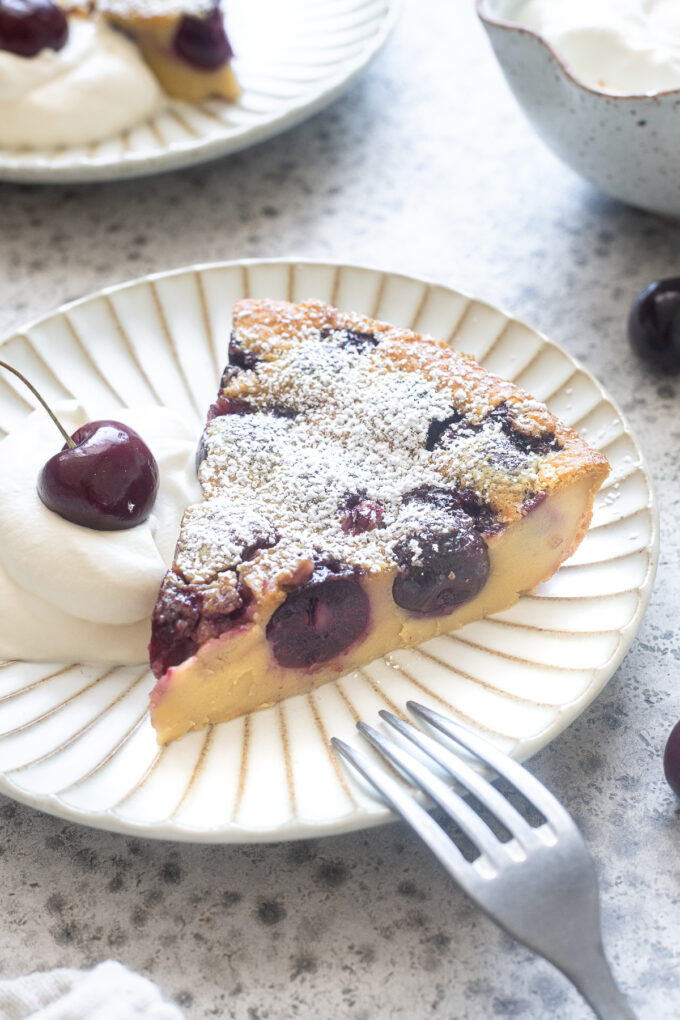 Slice of cherry clafoutis on a plate with whipped cream.