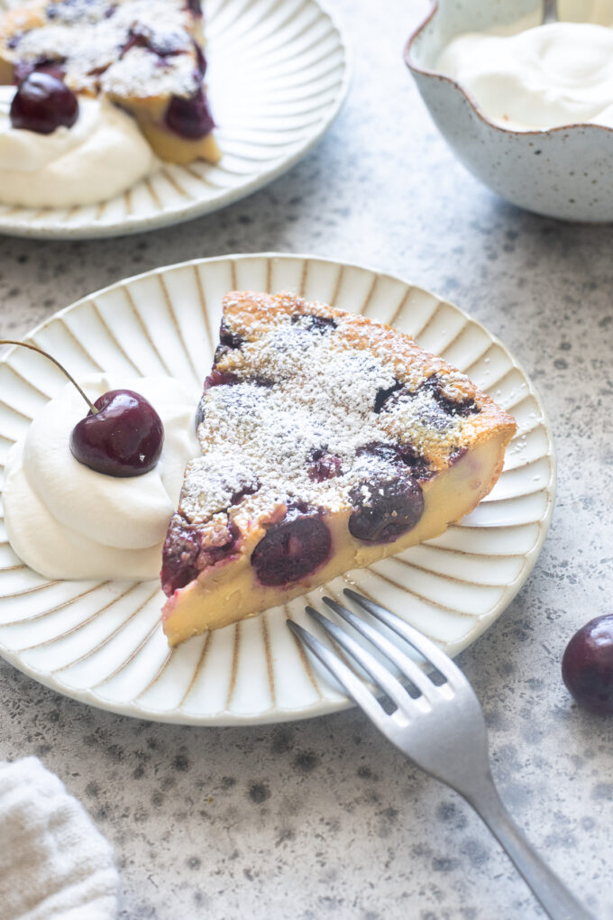 Slice of Cherry clafoutis on a plate with whipped cream.