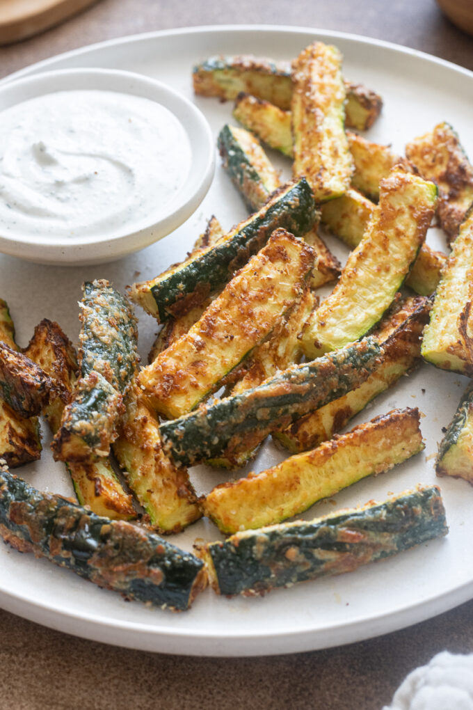 Golden brown air fryer zucchini fries coated in parmesan cheese with a side of Greek yogurt ranch.